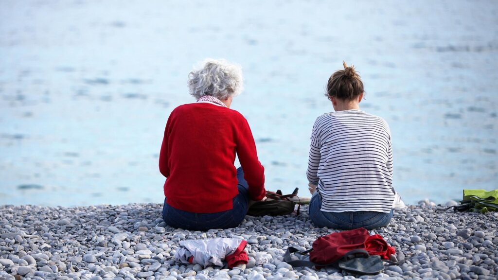 Alte und junge Frau sitzen am Strand