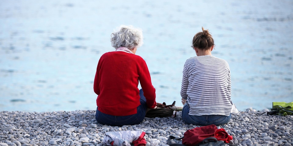 Alte und junge Frau sitzen am Strand