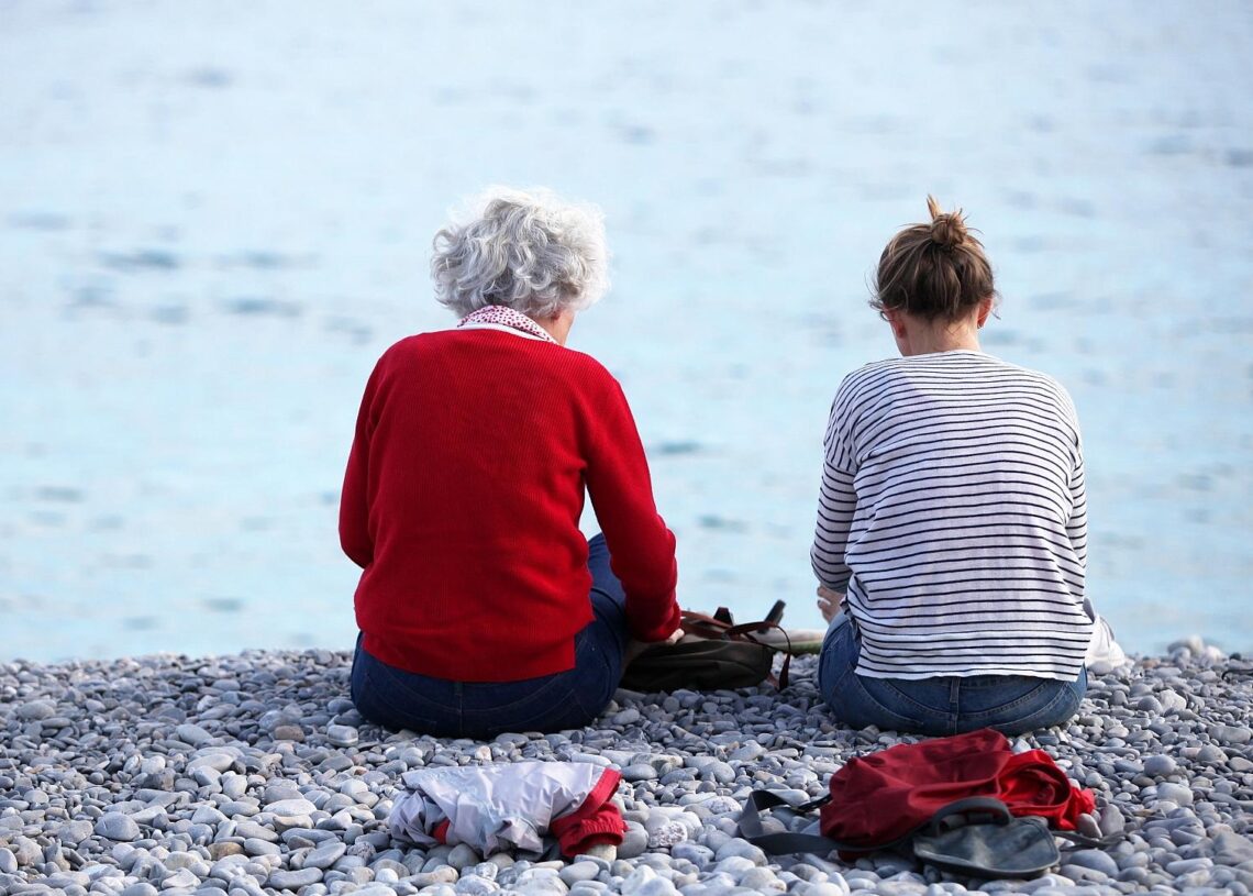 Alte und junge Frau sitzen am Strand