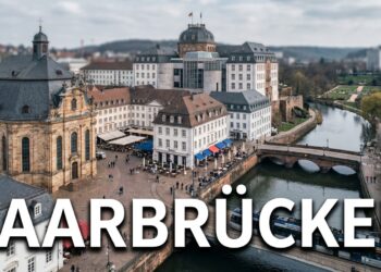 Stadtansicht der Landeshauptstadt Saarbrücken mit der barocken Ludwigskirche als Wahrzeichen oder dem Saarbrücker Schloss mit seinem charakteristischen modernen Mittelbau (Gottfried Böhm). Alternativ: St. Johanner Markt mit seiner lebendigen Fußgängerzone und französischem Flair, die Alte Brücke zwischen Alt-Saarbrücken und St. Johann, oder der Deutsch-Französische Garten als grüne Lunge. Architektonische Mischung aus barockem Erbe (Stengel-Bauten) und moderner Stadtentwicklung. Dezenter Hinweis auf die Grenznähe zu Frankreich durch französisch inspirierte Elemente (Café-Kultur, Saarbahn-Trasse Richtung Sarreguemines). Der Schriftzug "SAARBRÜCKEN" in großen, modernen Lettern, klare serifenlose Schrift, weiß mit dunklem Schatten für Lesbarkeit. Atmosphäre: Metropolitan, kulturell vielfältig, grenzüberschreitend, barock-modern.