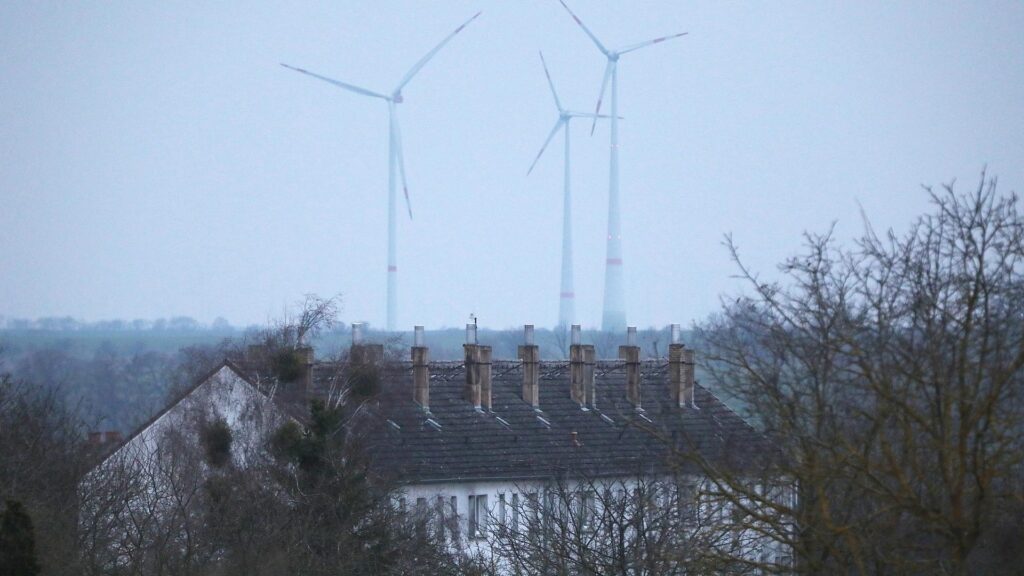 Ein Mehrfamilienhaus mit Windrädern im Hintergrund (Archiv)