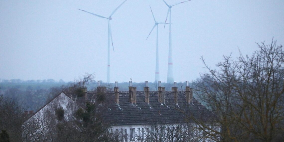 Ein Mehrfamilienhaus mit Windrädern im Hintergrund (Archiv)