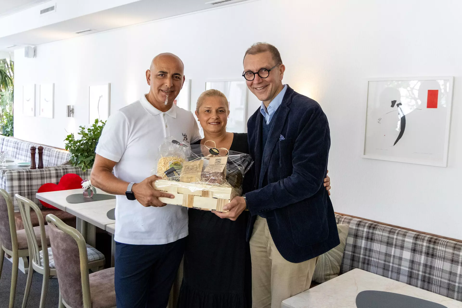 Café Stube St. Ingbert feiert 30-jähriges Bestehen 1 Aktuelles aus St. Ingbert | Bild: Stadt St. Ingbert Drei Personen stehen in einem bestuhlten Raum und halten gemeinsam einen Präsentkorb.